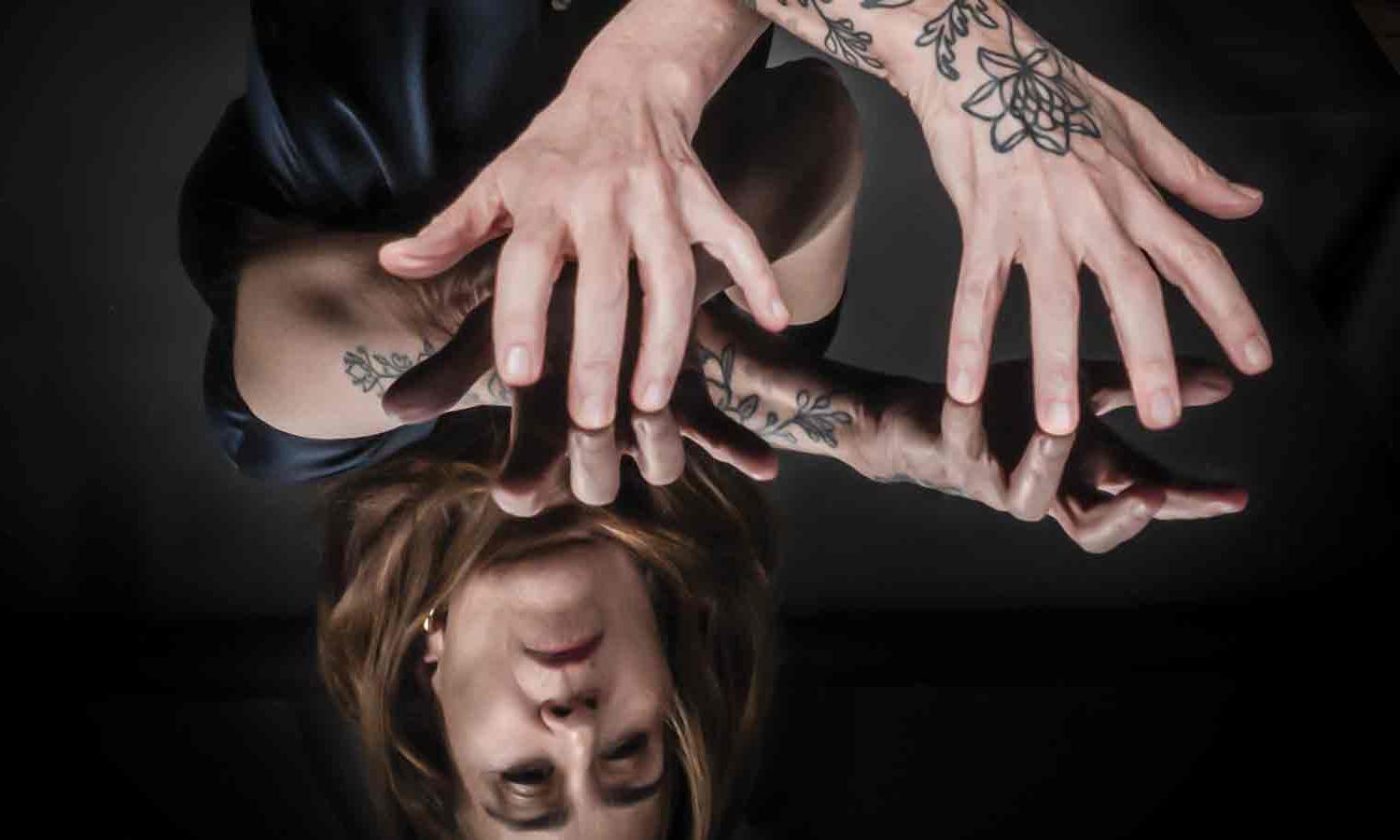 Photo of Jeanine Tesori ’83, her face and tattooed arms and hands reflected in a mirrored tabletop