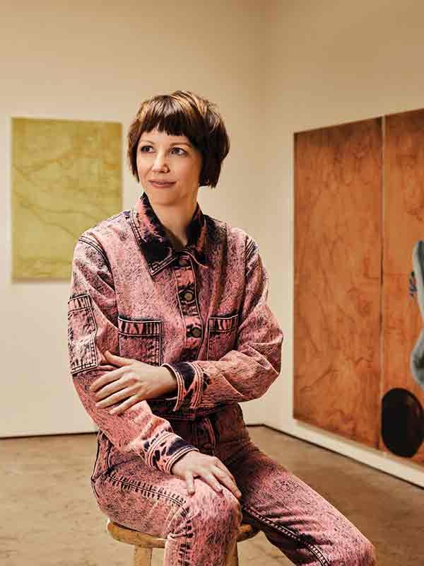 Jesse Mockrin sitting on a stool in an art gallery wearing a dark-pink denim outfit