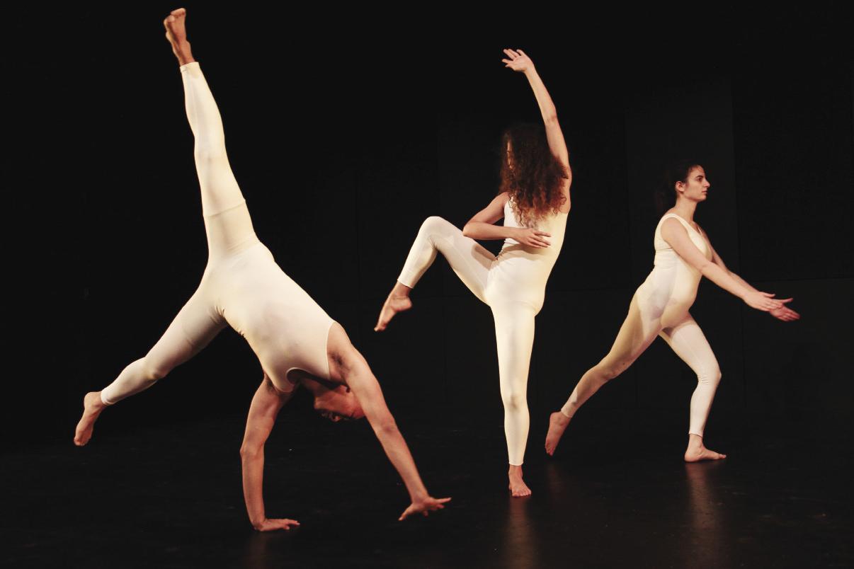 3 people in white body suits dancing on a black stage