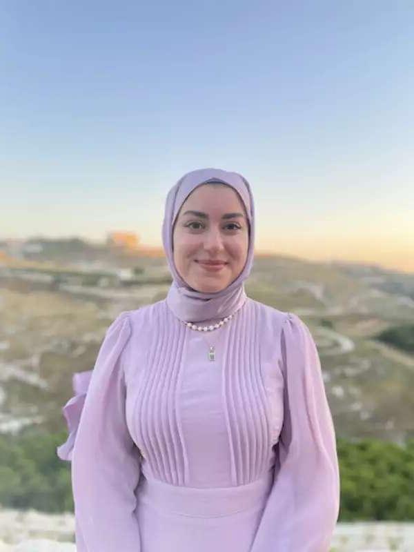 A woman in a pink outfit stands in front of a landscape at sunset. 